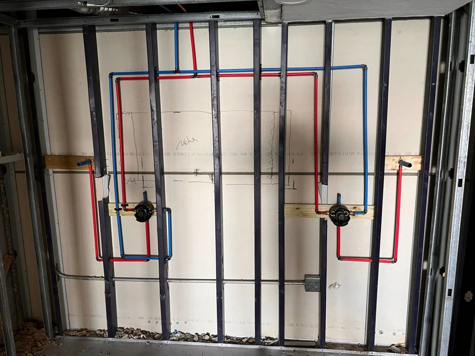 Shower valve rough-in with visible PEX supply lines, drains and metal framing